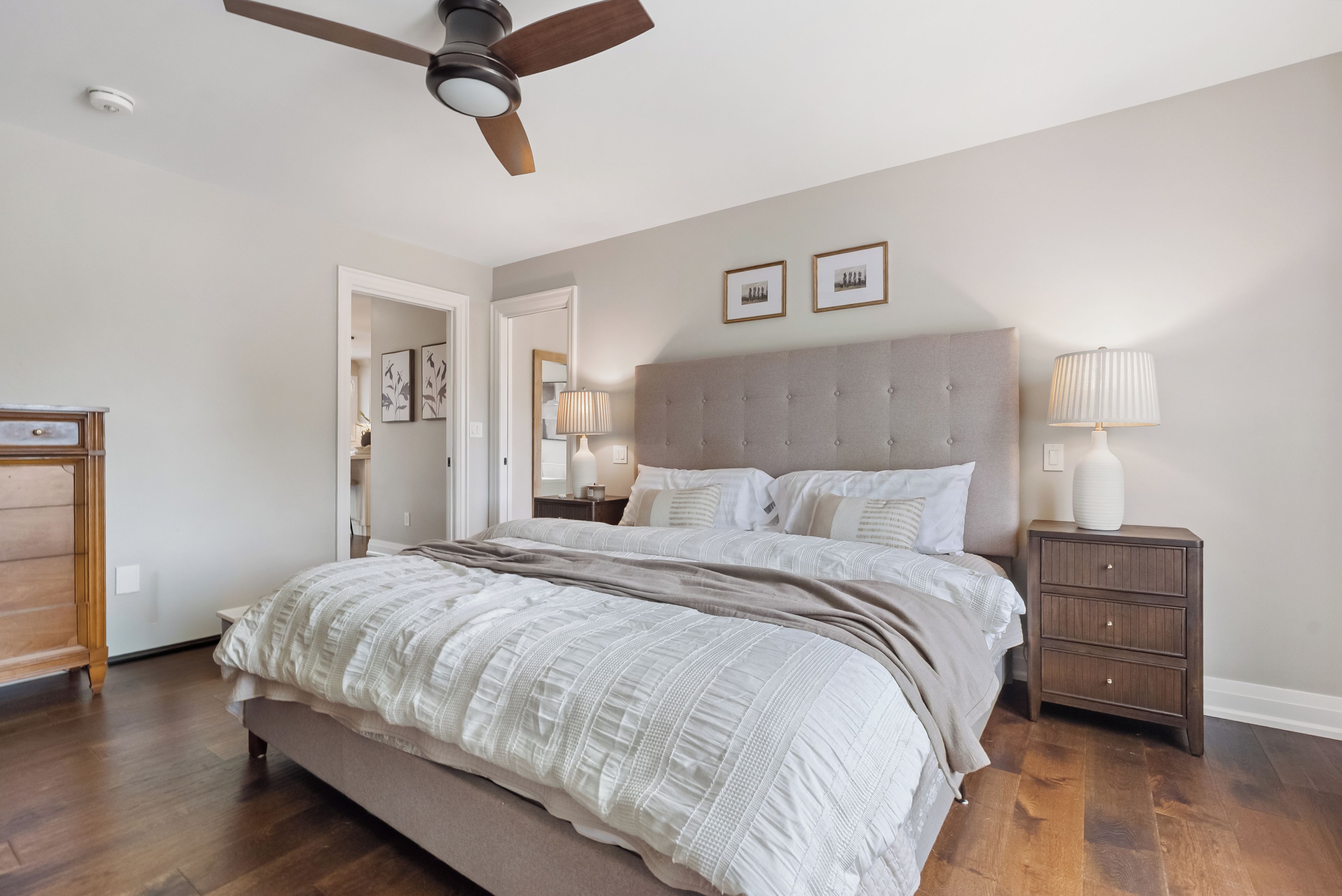 Une chambre avec un grand lit, un ventilateur de plafond, une table de chevet avec une lampe et une commode.