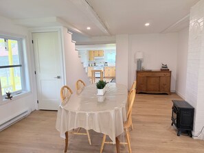 A dining area with a round table, chairs, and a potted plant. A kitchen is visible in the background. - Charming country cottage (Sainte-Sabine)