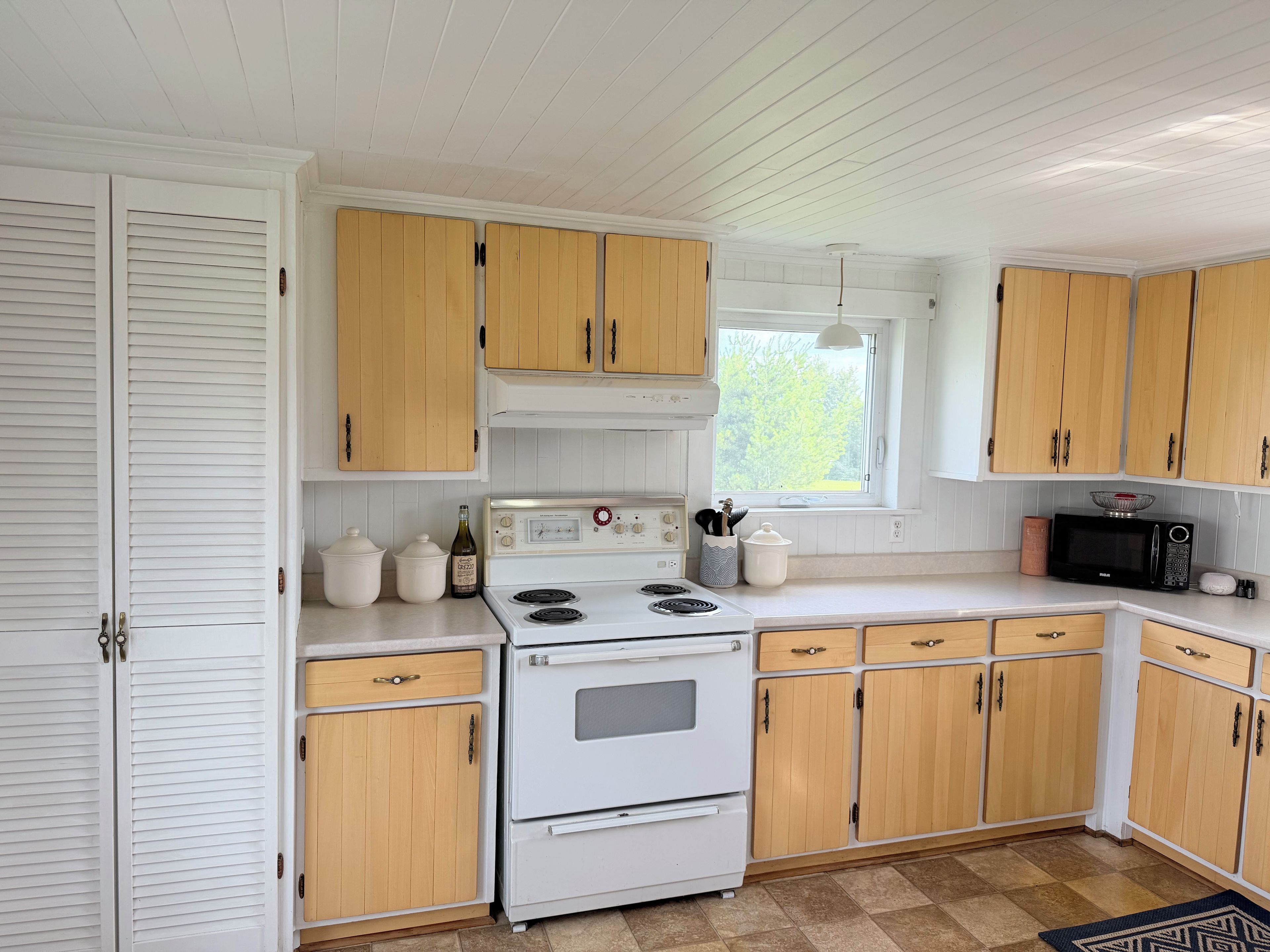 A kitchen with white cabinets, a stove, a microwave, and a window.