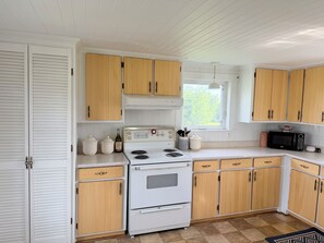 Une cuisine avec des meubles blancs, une cuisinière, un four à micro-ondes et une fenêtre.