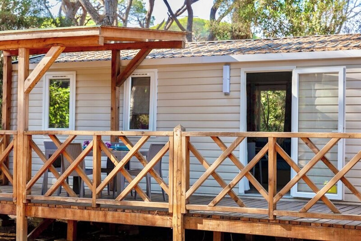 Eine Holzterrasse mit Geländer, einem überdachten Bereich und einem Gebäude mit Fenstern und Türen.