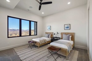 A bedroom with two beds, a ceiling fan, and a large window with a mountain view. - Four Seasons Estate for up to 20 with Lake and Ski Access (Heber city)