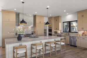 A modern kitchen with a large island, bar stools, pendant lighting, and a view of the outside. - Four Seasons Estate for up to 20 with Lake and Ski Access (Heber city)