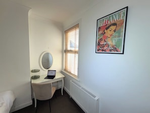 A bedroom with a bed, a desk with a laptop, a mirror, a radiator, and a poster on the wall. - Family & Work Stay | Garden, Parking & Workspace (Southend-on-Sea)