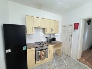 A compact kitchen with a black refrigerator, a microwave, and a gas stove. - Family & Work Stay | Garden, Parking & Workspace (Southend-on-Sea)