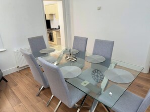 A modern dining area with a glass table and grey upholstered chairs. - Family & Work Stay | Garden, Parking & Workspace (Southend-on-Sea)