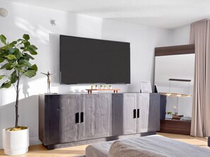 A modern living room with a flat-screen TV mounted on the wall, a dark wooden cabinet with a plant, and a large mirror reflecting the room. - Brickell Condo w Pool, Parking & Balcony (Miami)