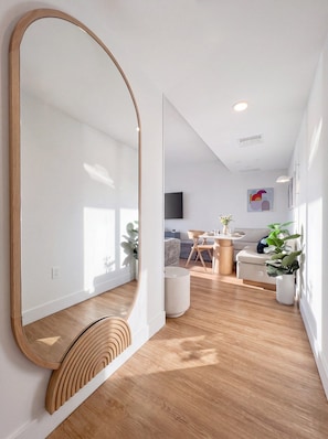A modern living room with a large mirror, wooden flooring, and a dining area with a table and chairs. - Luxury Downtown Miami Condo w Pool & Views (Miami)