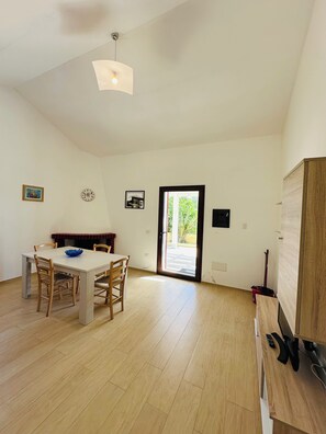 Um quarto amplo com mesa e cadeiras de jantar, um armário de madeira e uma porta de vidro deslizante que dá para uma área externa.