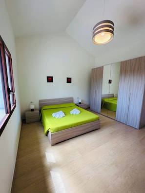 Quarto moderno com cama, mesas de cabeceira, espelho e janela.