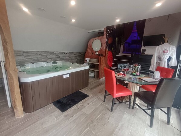 A modern bathroom with a hot tub, a mirror, and a dining area with red chairs and a table.