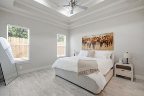 A bedroom with a bed, a ceiling fan, two bedside tables with lamps, and a large painting on the wall. - The Oak House - Love Street Collection 
Luxury New Build Near Love St. Park (Weatherford)