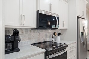 Cocina moderna con armarios blancos, microondas integrado, cafetera Keurig y refrigerador de acero inoxidable.