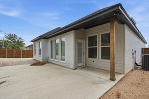 A single-story house with a covered patio, a fenced backyard, and a clear sky. - The Oak House - Love Street Collection 
Luxury New Build Near Love St. Park (Weatherford)