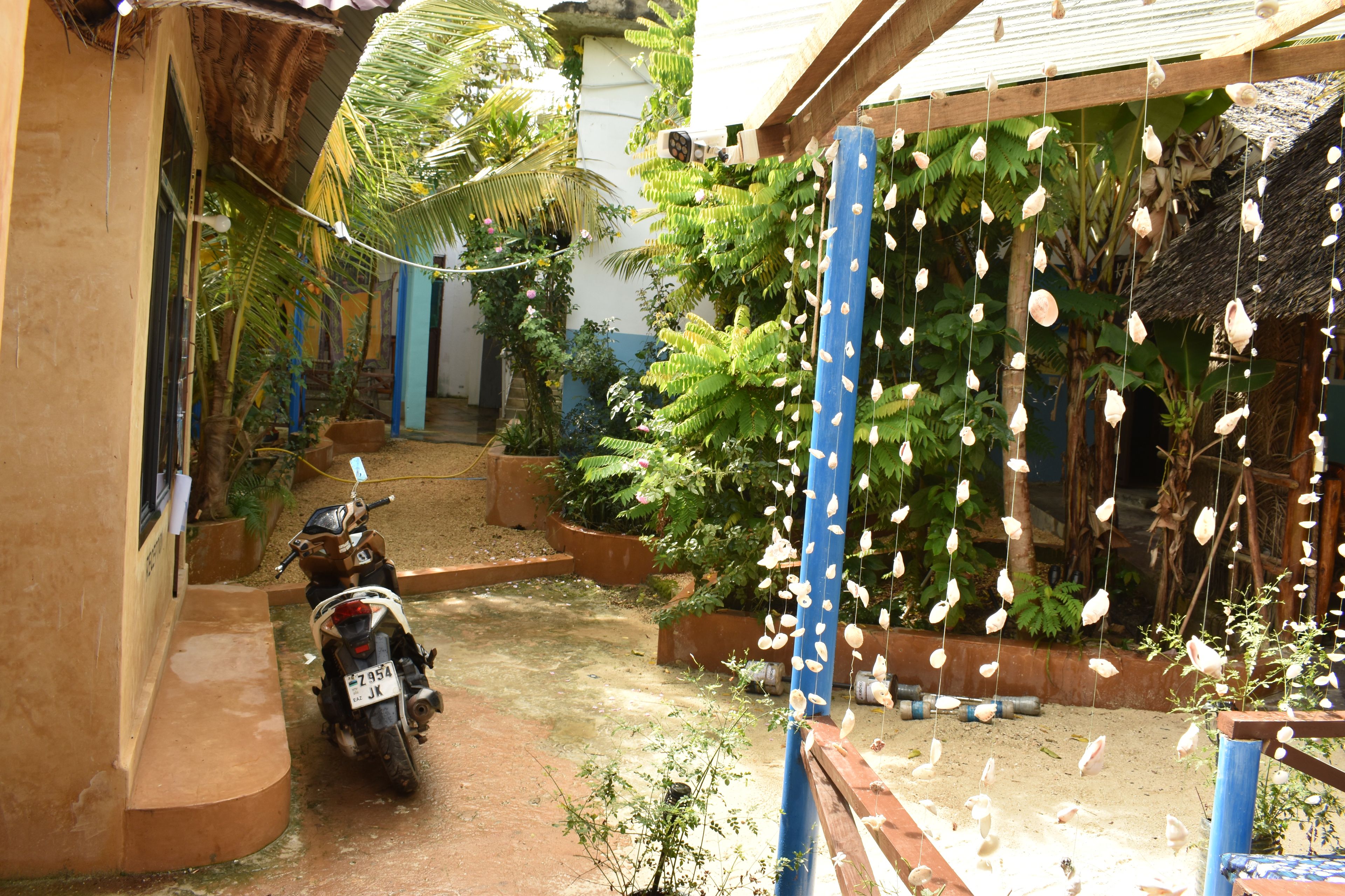 Una motocicleta estacionada en un jardín con una estructura azul y conchas colgantes.