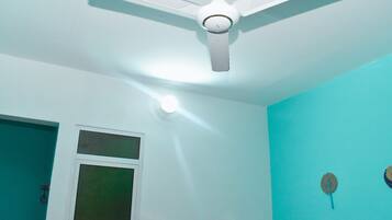 Una habitación con ventilador de techo blanco, ventana y paredes color esmeralda.