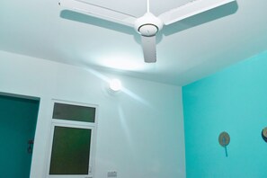 Una habitación con ventilador de techo blanco, ventana y paredes color esmeralda.