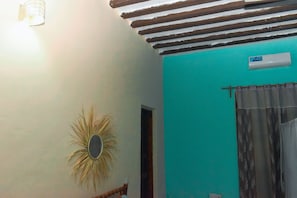 A room with a teal wall, a ceiling fan, a light fixture, a window with curtains, and an air conditioning unit.