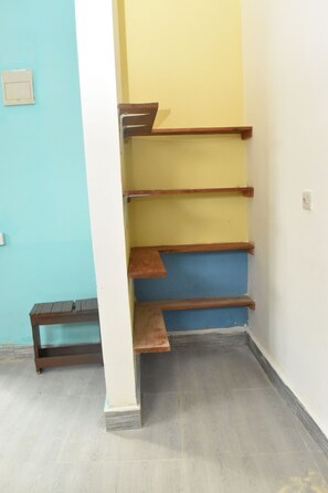 A corner of a room with a blue wall, a white column, and a wooden staircase with three steps.