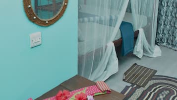Una habitación con una cama bajo una mosquitera, un espejo redondo en la pared, una mesa con un mantel colorido y una alfombra estampada.