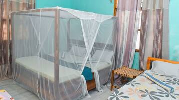 A room with a bed under a mosquito net, a small wooden stool, and a bed with a patterned bedspread.