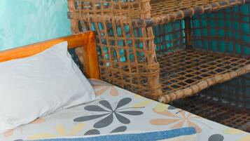 Una cama con colcha estampada, cabecera de madera y una silla de ratán trenzado frente a una pared color turquesa.