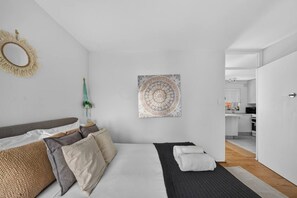 A modern bedroom with a bed, pillows, a wall hanging, and a view into the kitchen. - 1BR 1BA | Near to Beach, Manly’s shops, Cafés and Restaurants (Manly)