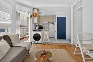 A compact living space with a sofa, a coffee table, a washing machine, and a blue door. - 1BR 1BA | Near to Beach, Manly’s shops, Cafés and Restaurants (Manly)