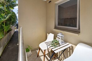 A small outdoor seating area with a table and two chairs, a potted plant, and a window with blinds. - 1BR 1BA | Near to Beach, Manly’s shops, Cafés and Restaurants (Manly)