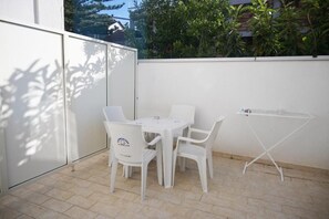 An outdoor patio with a white table and chairs, a drying rack, and a view of greenery and buildings in the background. - Oro Blu (BAGNARA CALABRA)