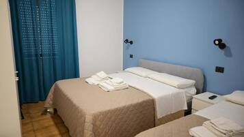 A hotel room with two beds, a blue wall, and a door with curtains.
