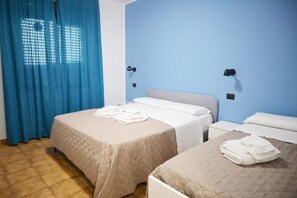 A hotel room with two beds, a blue wall, and a window with curtains.