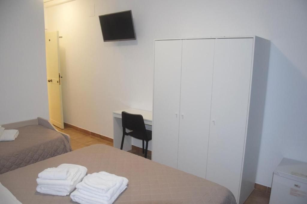 Quarto de hotel com duas camas, uma escrivaninha, uma cadeira, um guarda-roupa e uma televisão na parede.