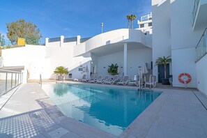 A swimming pool with sun loungers and a lifebuoy, surrounded by a white building with a curved roof and palm trees. - Holiday Home in Nerja With Sea Views (Nerja)