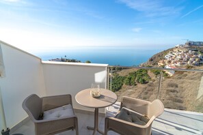 A balcony with wicker furniture and a glass table, overlooking a coastal town and the sea. - Holiday Home in Nerja With Sea Views (Nerja)
