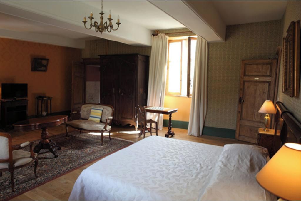 A hotel room with a large bed, a desk, a chair, a television, and a wardrobe.