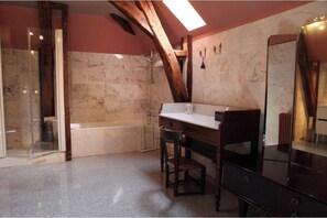 Un baño con bañera, cabina de ducha de vidrio, un escritorio de madera y un espejo grande.