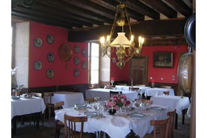 A dining area with round tables set for service, a chandelier, and a red wall with decorative plates.