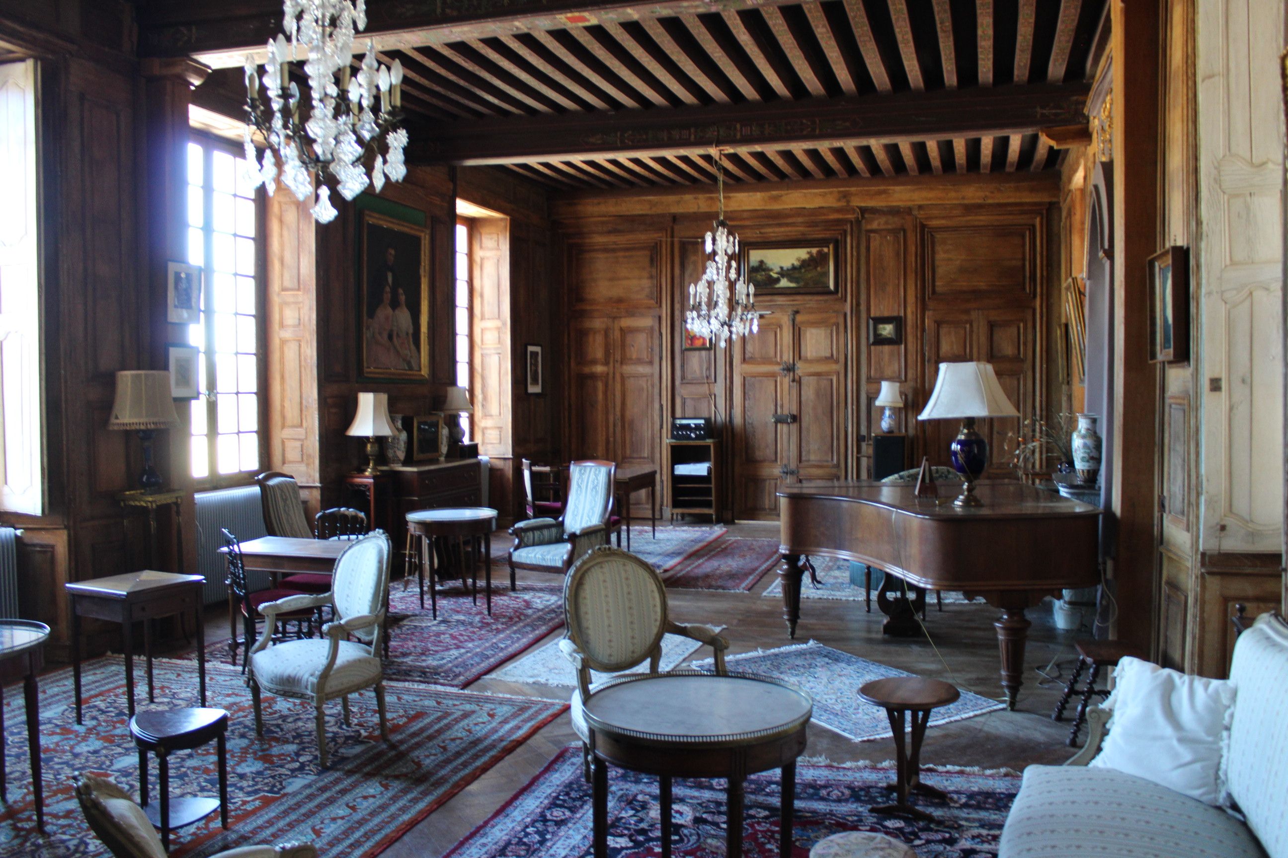 Une pièce spacieuse avec des boiseries, un grand piano, de nombreux fauteuils et un lustre.