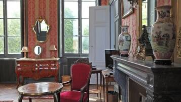 Une pièce avec une cheminée, un fauteuil rouge, une table en bois et un miroir.