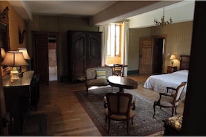 Habitación de hotel con cama, dos sillones, una mesita, un escritorio con lámparas y un armario grande.