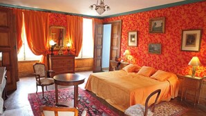 Ein Zimmer mit einem Bett, einem Schminktisch, einem Sessel, einem Tisch und einer Lampe.