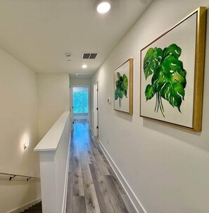 Ein Flur mit einer Treppe, Holzboden und gerahmten Kunstwerken an den Wänden.