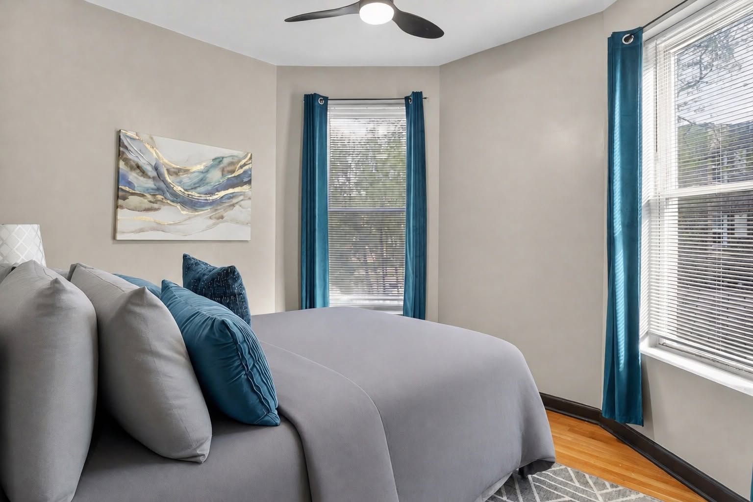 A bedroom with a bed, a ceiling fan, a window with blinds, and a painting on the wall.