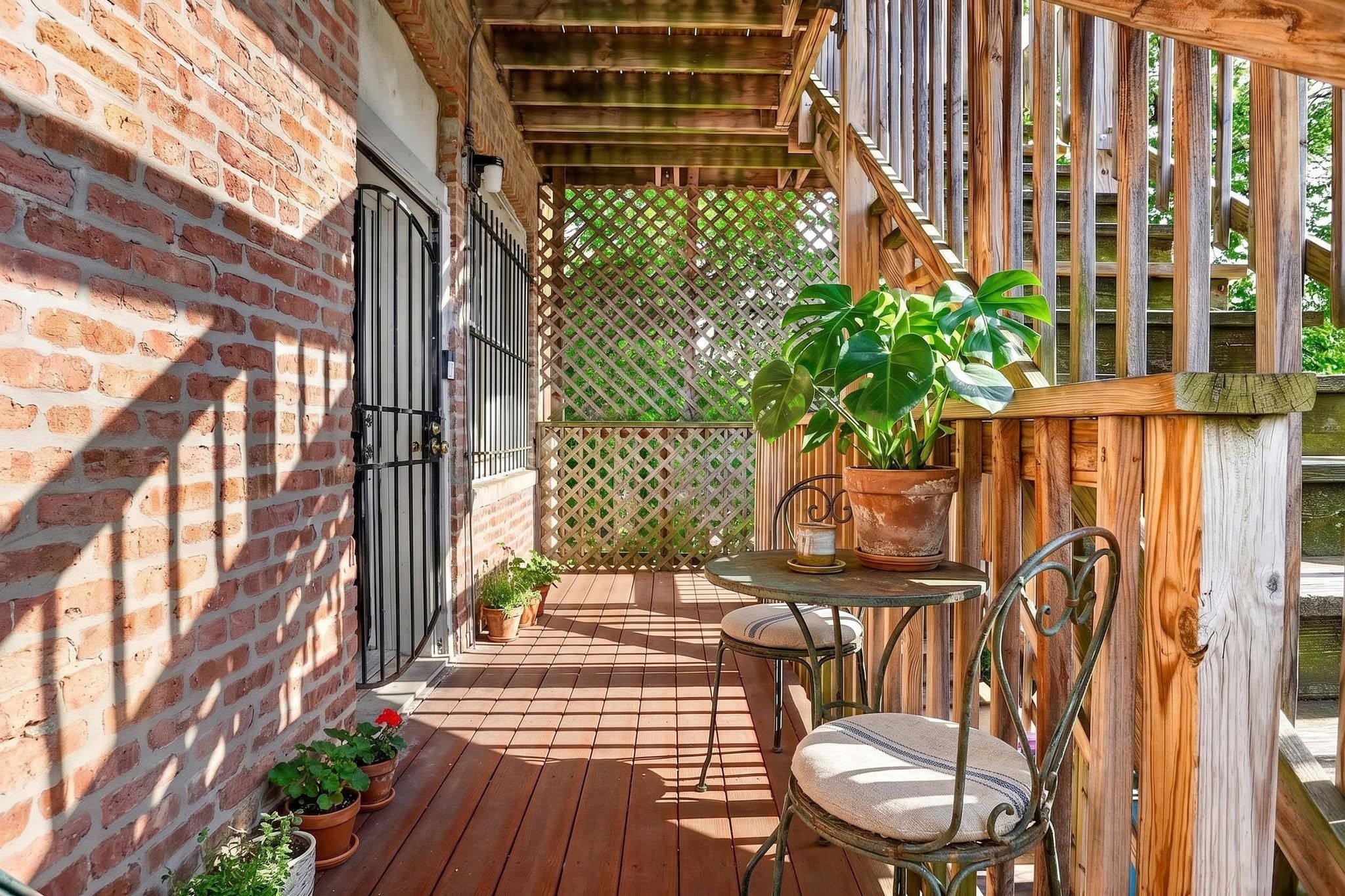 A wooden deck with a brick wall, a metal gate, and potted plants.