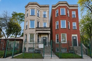 A row of two-story townhouses with a shared entrance, each with a number plaque, a small front yard, and a green metal fence. - Charming 3BR/2BA condo near Hyde Park (Chicago)