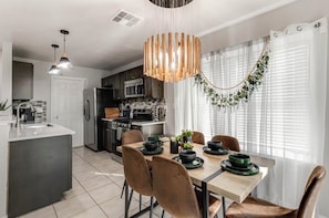 A modern kitchen with a dining area, featuring a central island, pendant lights, and a decorative plant arrangement. - Spacious & tranquil 4-bedroom house 20min Airport, Fort Sam &Downtown SanAntonio (San Antonio)