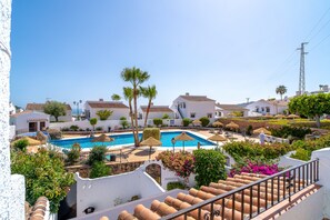 A pool area with a clear blue pool, surrounded by white buildings with terracotta roofs, palm trees, and a staircase leading to a terrace. - Capistrano Village Sundreams by Casasol (Nerja)