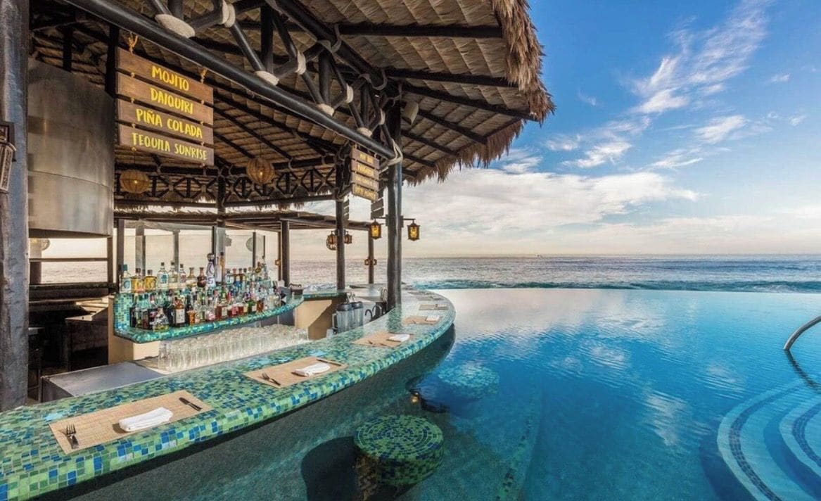 An infinity pool with a bar area and a thatched roof structure.