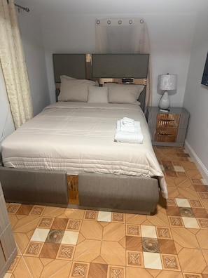Ein ordentlich bezogenes Bett mit Kopfteil, ein Nachttisch mit Lampe und ein gemusterter Boden.